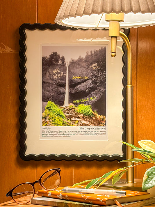 Framed picture of a waterfall with text on a wooden surface next to a lamp and glasses.