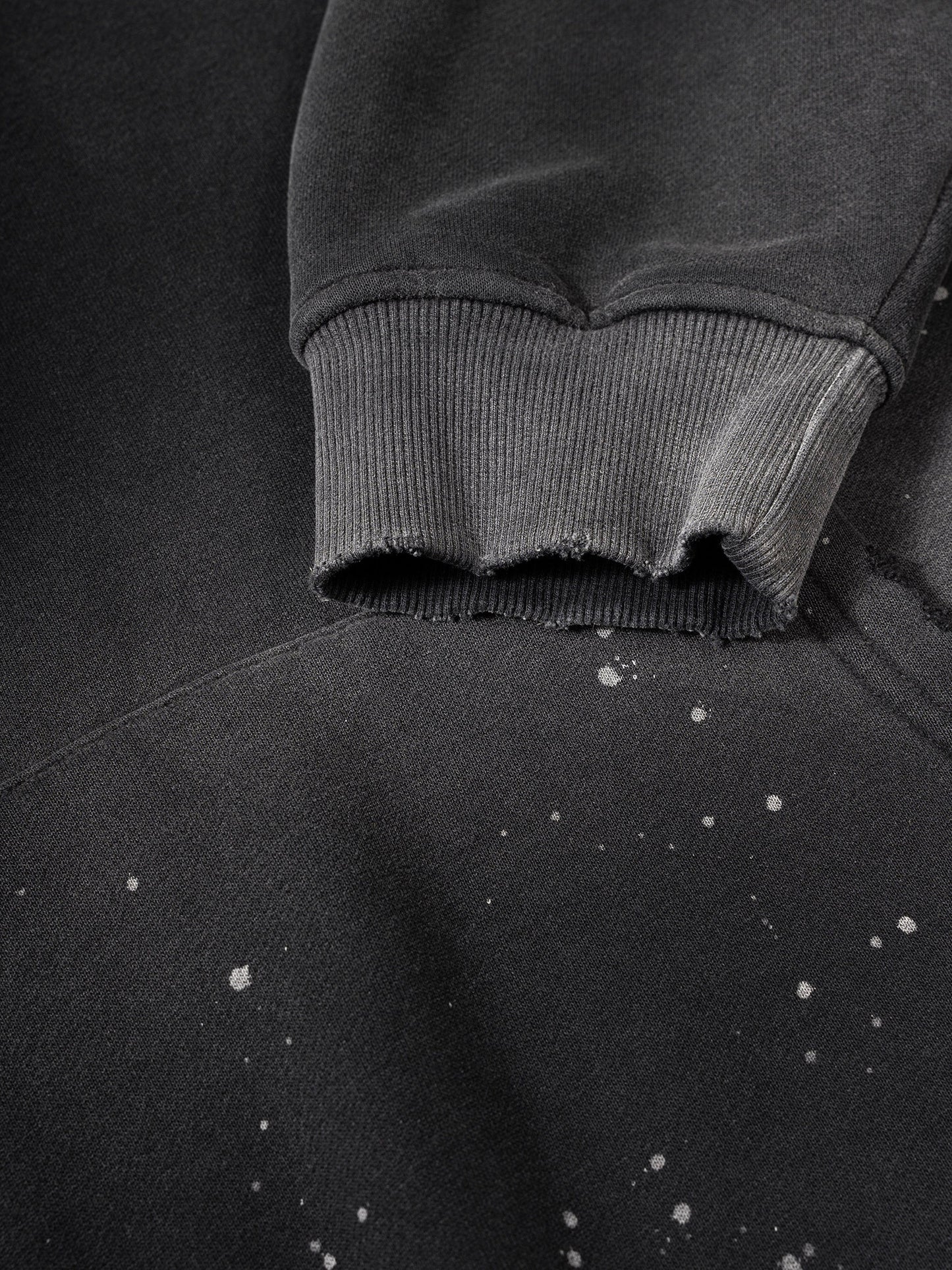 Close-up of a dark gray sweatshirt with frayed hem on a matching background