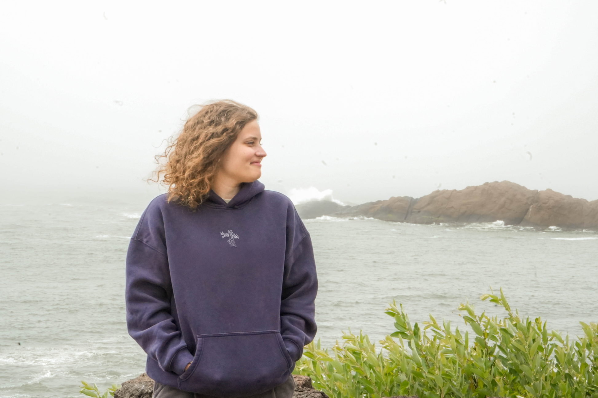 Person wearing a purple hoodie standing by a body of water with foggy background
